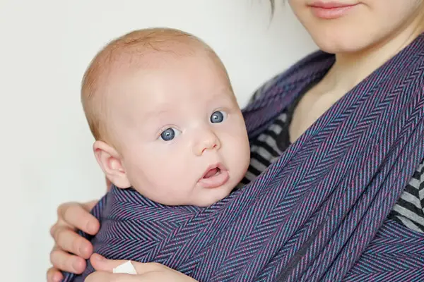 Mutter macht Kanga-Training zu Hause mit ihrem Baby im Tragetuch, stärkt ihre Fitness und genießt die Nähe zum Kind.